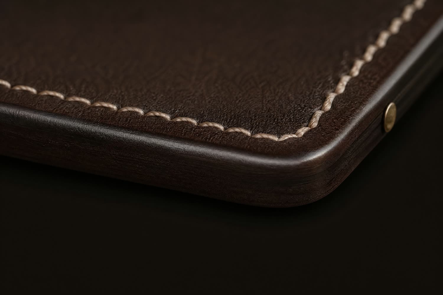 Macro of a sanded and burnished cut edge on thick espresso leather, glossy against the matte grain above it