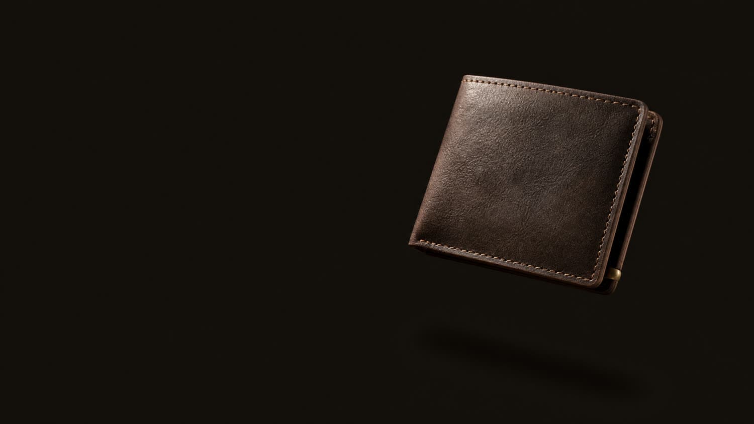 An espresso full-grain leather bifold wallet suspended against a dark ground, lit hard from one side